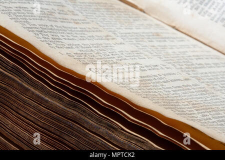 An old, antique (19th century) English Bible lying open in the Psalms, with some faded pages, and with some of the edge pages and center visible. Stock Photo