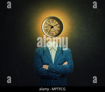 Surreal image of a serious professor with crossed hands and a clock instead of his head over chalkboard background. The concept of time in educational Stock Photo