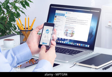 Telegram messenger on iPhone screen in male hands and desktop version of Telegram on macbook. Stock Photo