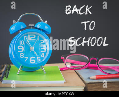 Back to school concept. Alarm clock on stacks of books with pink glasses and red pencil  on  wooden table and black background. Stock Photo