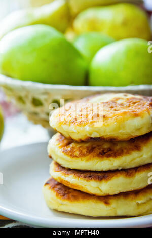 Stack of Homemade Scrumptious Cottage Cheese Pancakes Patties on White Plate. Apples Pear in Wicker Basket. Rustic Provence Style Kitchen Interior. Mo Stock Photo