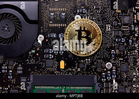 An Bitcoin physical coin sitting on a computer motherboard with a fan and RAM. It is the first decentralized currency Stock Photo