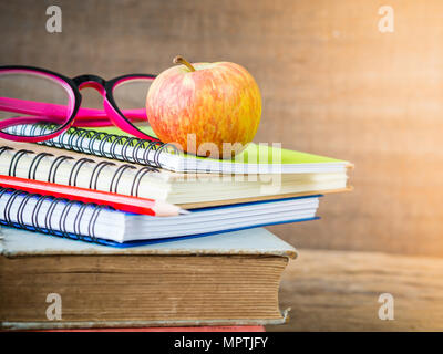 Back to school concept. Retro style of apple on stacks of books with pink glasses and red pencil on  wooden table background. Stock Photo