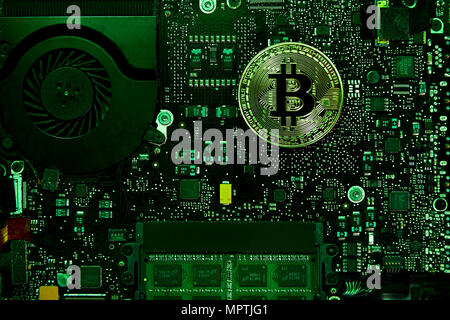 An Bitcoin physical coin sitting on a computer motherboard with a fan and RAM.  Green Light covers the scene.  Using the public domain logo. Stock Photo