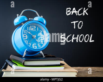 Back to school concept. Alarm clock on stacks of books on  wooden table and black background. Stock Photo