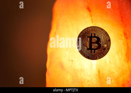 A physical gold Bitcoin with the public domain logo sits on a Himalayan sea salt crystal with a glowing warm light radiating. Stock Photo