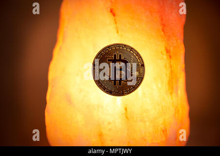A physical gold Bitcoin with the public domain logo sits on a Himalayan sea salt crystal with a glowing warm light radiating. Stock Photo