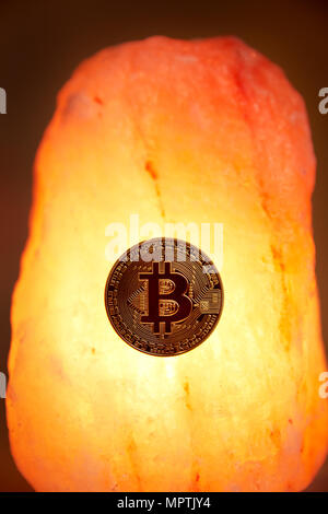 A physical gold Bitcoin with the public domain logo sits on a Himalayan sea salt crystal with a glowing warm light radiating. Stock Photo