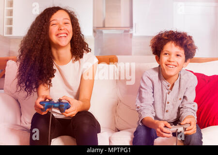 Portrait of age-diverse boy and girl, happy friends, sitting on the sofa at home, playing video games together Stock Photo