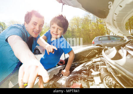 Portrait of happy young father and little boy pointing with their fingers on broken part of car engine during motor maintenance Stock Photo