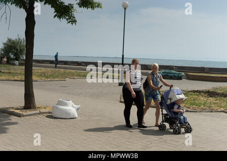Two women with a child are walking along the embankment on a sunny summer day Stock Photo
