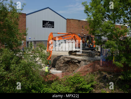 360 tracked hydraulic excavator lifting concrete blocks onto new flood wall on river bank, protecting industrial buildings on the river irwell bury uk Stock Photo