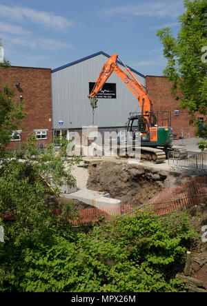 360 tracked hydraulic excavator lifting concrete blocks onto new flood wall on river bank, protecting industrial buildings on the river irwell bury uk Stock Photo