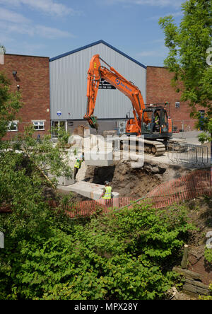 360 tracked hydraulic excavator lifting concrete blocks onto new flood wall on river bank, protecting industrial buildings on the river irwell bury uk Stock Photo