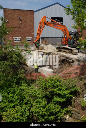 360 tracked hydraulic excavator lifting concrete blocks onto new flood wall on river bank, protecting industrial buildings on the river irwell bury uk Stock Photo