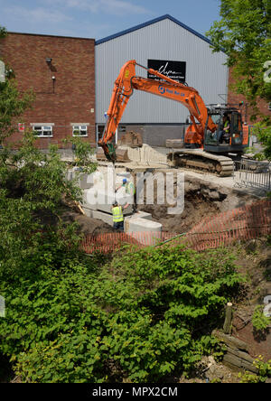 360 tracked hydraulic excavator lifting concrete blocks onto new flood wall on river bank, protecting industrial buildings on the river irwell bury uk Stock Photo