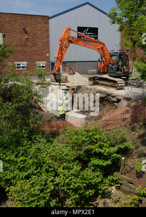 360 tracked hydraulic excavator lifting concrete blocks onto new flood wall on river bank, protecting industrial buildings on the river irwell bury uk Stock Photo