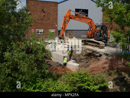 360 tracked hydraulic excavator lifting concrete blocks onto new flood wall on river bank, protecting industrial buildings on the river irwell bury uk Stock Photo