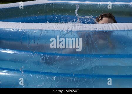 Inflatable paddling pool: a unidentifiable boy playing with a garden hose in an inflatable paddling pool Stock Photo