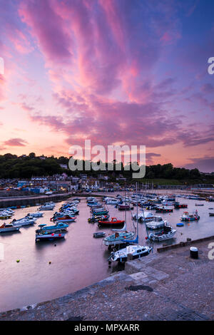 At sunset pink and red hues reflect off the clouds above the boat filled Cobb harbour at Lyme Regis on the Jurassic Coast of Dorset on 23rd May 2018. 