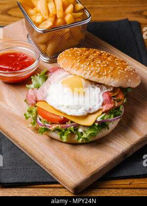 Close-up of burger with French Fries and ketchup served on wooden cutting board Stock Photo