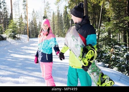 Couple holding hands while standing on snow covered field in forest Stock Photo