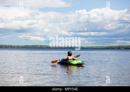 Rear view of boy kayaking in lake against cloudy sky Stock Photo