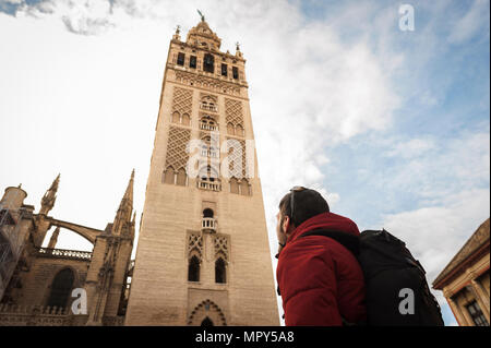 Low angle view of backpacker looking at La Giralda in Seville Cathedral against cloudy sky in city Stock Photo