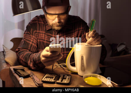 Man wearing protective eyewear while repairing appliance using smart phone at home Stock Photo