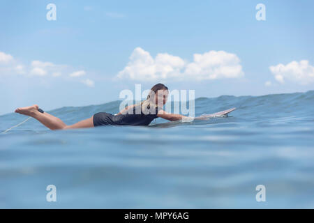 Full length portrait of carefree smiling woman lying on surfboard while swimming in sea Stock Photo