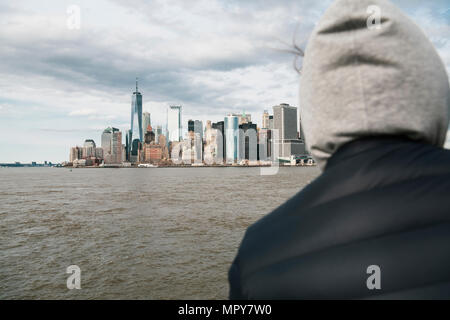 Rear view of woman looking at modern buildings while standing by river against cloudy sky Stock Photo