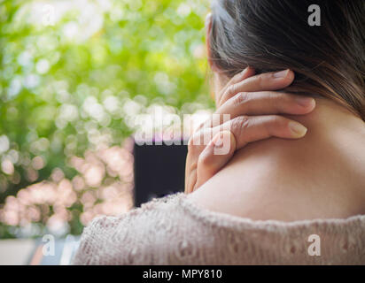 Woman put her hand on the back of her neck while feeling pain after long hours work on computer. Office syndrome concept. Stock Photo