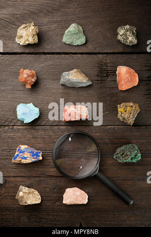 Overhead view of colorful gemstones with magnifying glass on wooden table