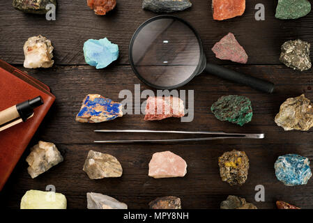 Overhead view of colorful gemstones with magnifying glass and tweezers on wooden table Stock Photo