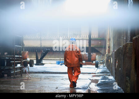 Rear view of manual worker wearing raincoat and helmet while walking at factory Stock Photo