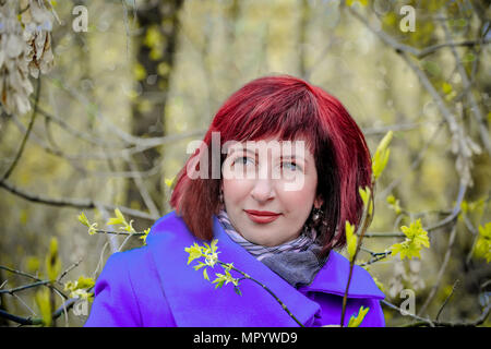 The girl with red hair in purple coat in the spring forest Stock Photo