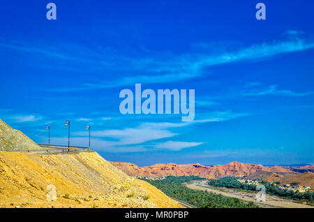 Clear blue sky over a winding road in the countryside with mountains in the distance. Shot from Muscat, Oman. Stock Photo