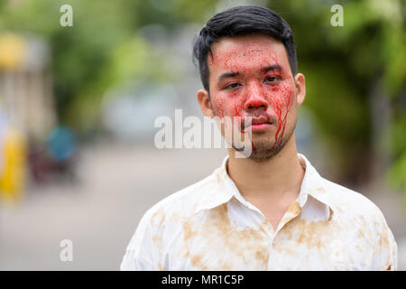 Young crazy Asian man with blood on face outdoors Stock Photo