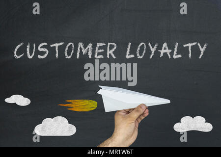 Customer loyalty on blackboard. Hand holding paper plane Stock Photo
