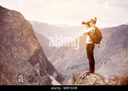 Photographer or traveller stands on big rock against mountains and taking photo Stock Photo