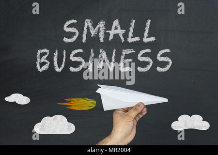 Hand holding paper plane and Small business words on blackboard. Stock Photo