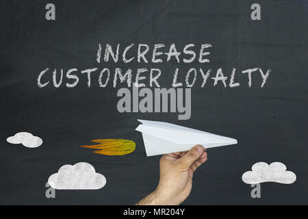 Increase customer loyalty concept on blackboard. Hand holding paper plane Stock Photo