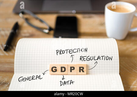 Closeup on notebook over wood table background, focus on wooden blocks with letters making GDPR General Data Protection Regulation text. Stock Photo