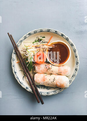 Asian style dinner. Flat-lay of steamed dumplings Dim sum and summer rice paper rolls with shrimp and sauce over blue table, top view, copy space. Chinese cuisine Stock Photo