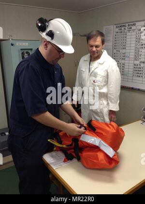 Petty Officer 1st Class Andrew Christopherson, a marine science technician at Coast Guard Marine Safety Unit Portland, inspects a personal floatation device for the required whistle and lights, during a Port State Control exam of the vessel Port Belmonte at the Port of Portland, Ore., May 1, 2017.    There must be adequate life jackets aboard for the crew members and safety equipment during an PSC exam. Stock Photo