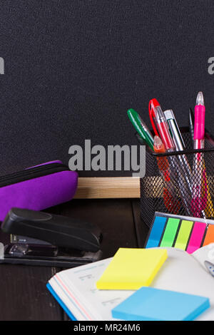Pencil case with various stationery on old wooden table, on blackboard background Stock Photo