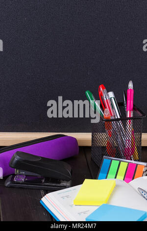 Pencil case with various stationery on old wooden table, on blackboard background Stock Photo