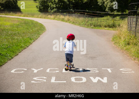 A four year old boy riding his scooter over a painted sign saying 'cyclist slow' in Bristol Stock Photo