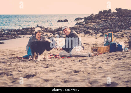 nice beautiful couple of male and female do a pic nic on the beach near thw wave with a dog border collie. love and friendship concept in summer vacat Stock Photo