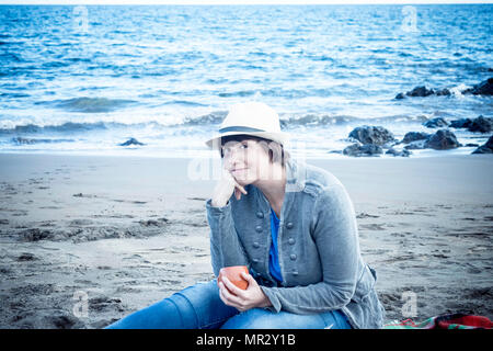 nice beautiful young lady smiling with hat sitting down at the beach in winter. vacation nice leisure concept outdoor. Stock Photo